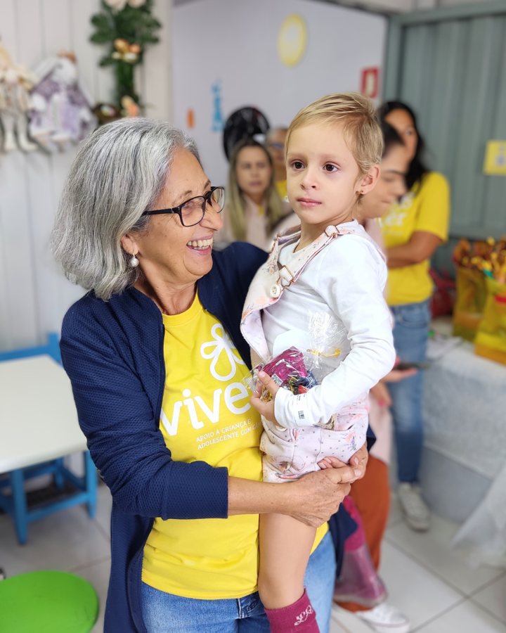 Voluntária da Viver segurando uma criança no colo, ambas sorrindo